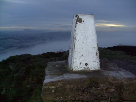 Trig point with heavily frosted base, cloud in the valley behind, at sunrise